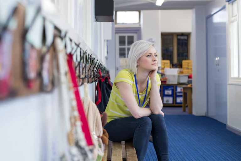 Teacher sitting on bench in cloakroom at school.