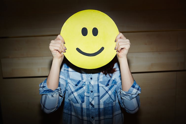 A woman holding a smiley face in front of her head.