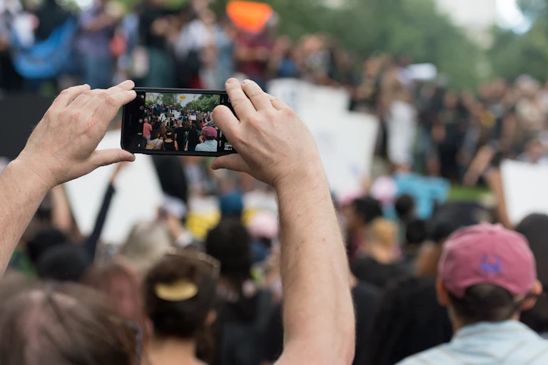 Man in crowd filming with smartphone