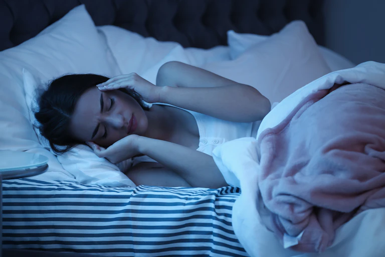A woman lying in bed with her hands on her head.