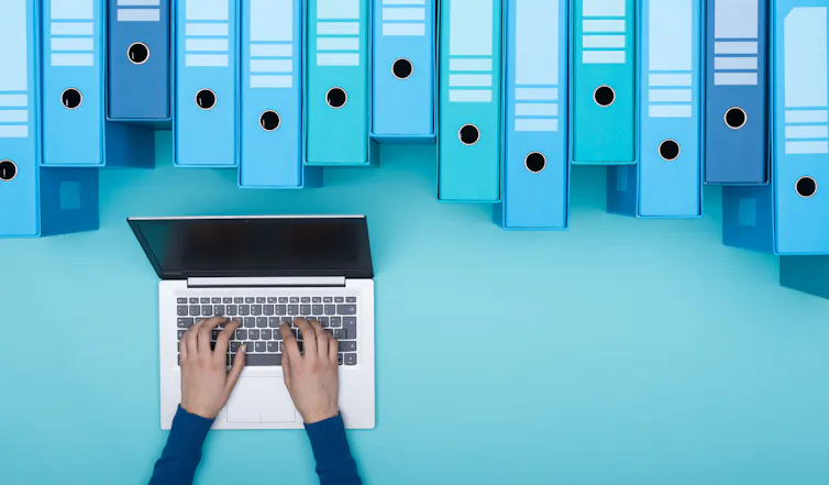 Hands on a laptop keyboard with box files.