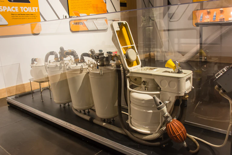 A display of a space toilet showing funnel, suction devices and four tanks to store waste.
