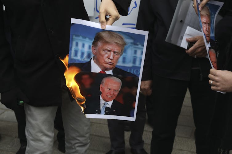 Protesters hold a burning photograph of Trump and Biden