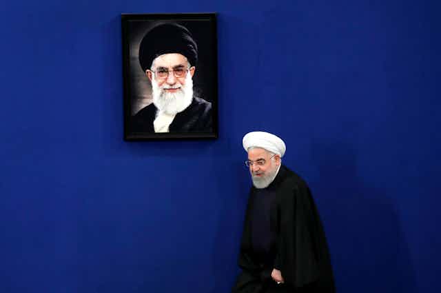 Iranian President Hassan Rouhani walks onto a stage with a portrait of the Supreme Leader Ayatollah Ali Khamenei hanging on the wall behind him. 