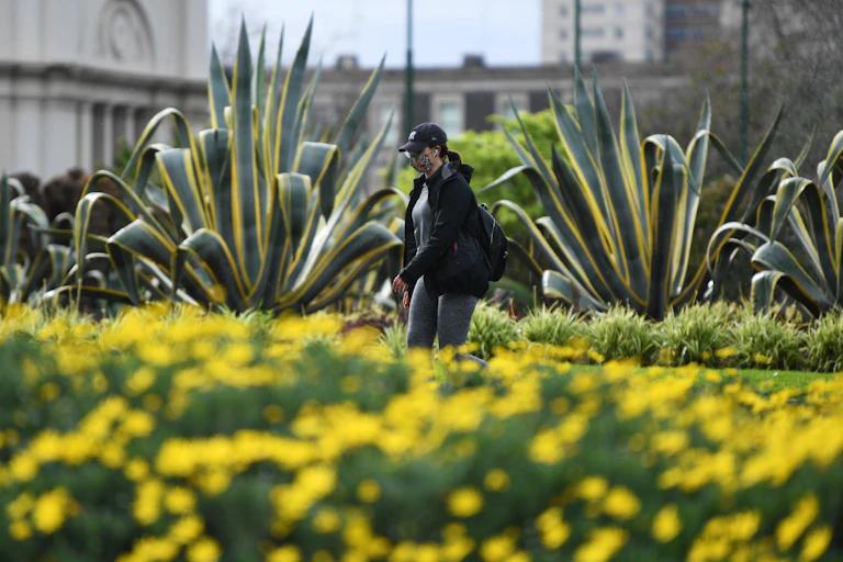 A lady, wearing a mask, walks through a garden