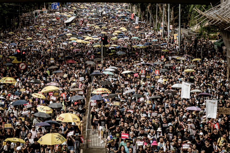 A large crowd of protesters, some holding umbrellas, on the streets of Hong Kong.