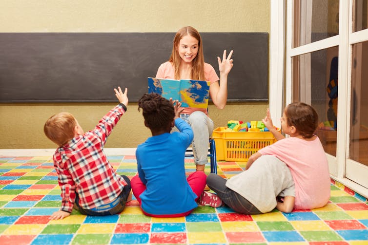 Woman reading out loud to three children in a classroom