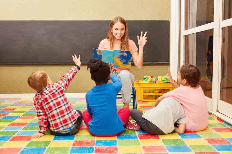 Woman reading out loud to three children in a classroom