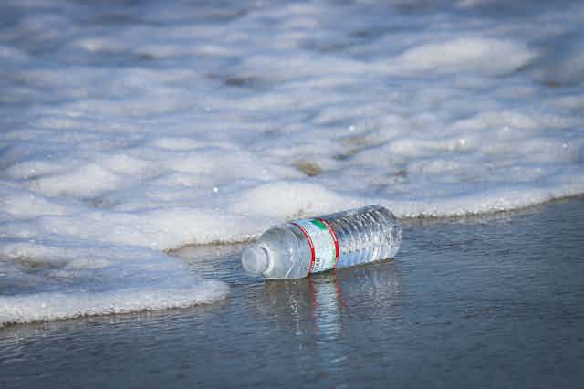 A plastic water bottle in the surf on a beach.