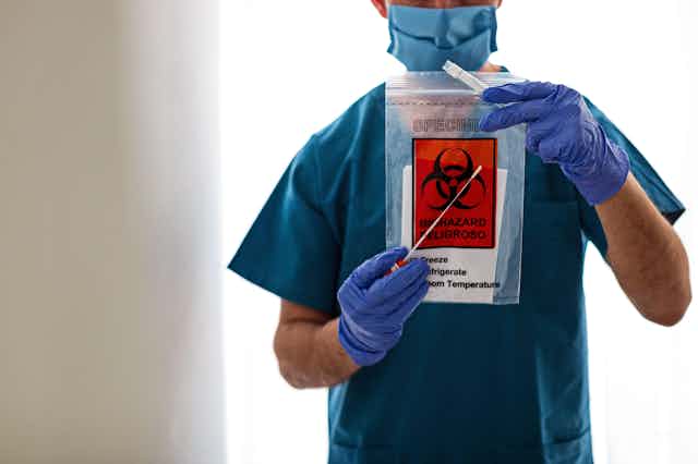 A medic holds a swab test kit up to the camera