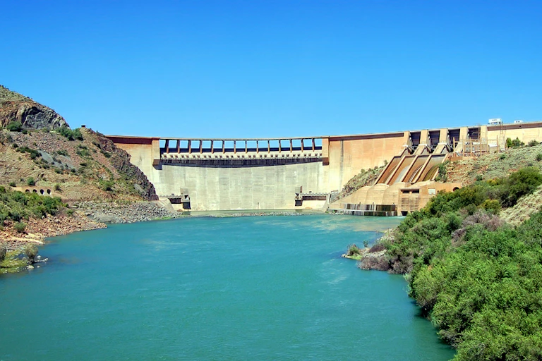 A dam in the Karoo, South Africa, surrounded by lush vegetation clear blue skies in the background.