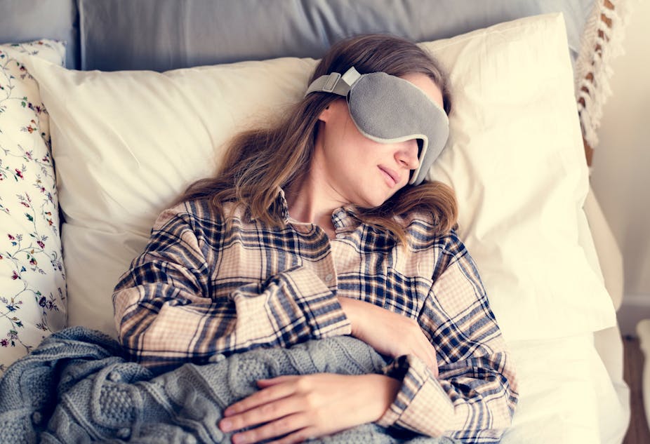 Woman napping in bed with sleep mask over her eyes.