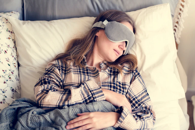 Woman napping in bed with sleep mask over her eyes.