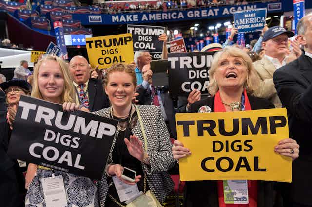 Three women hold 'Trump digs coal' signs at a rally