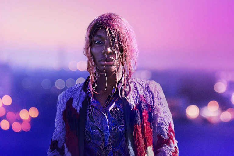 Young woman with wet pink hair with twinkling city behind.