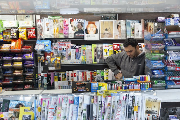 A newsagent surrounded by magazines and local papers.