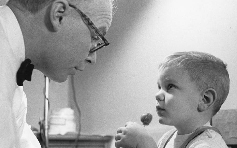 A little boy with a lollipop looks at a doctor.