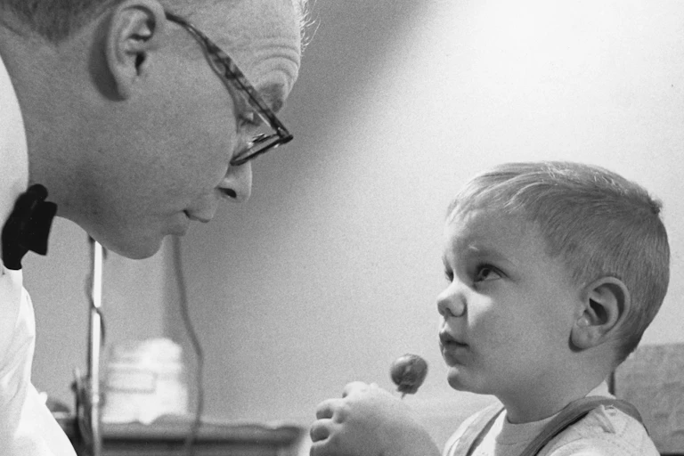 A little boy with a lollipop looks at a doctor.