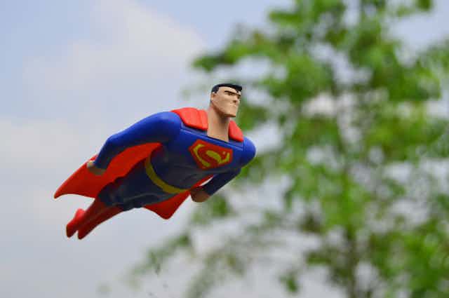 Toy Superman figurine flying past a tree.
