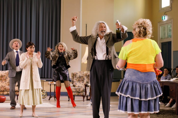 Production image: the cast parties in a hall