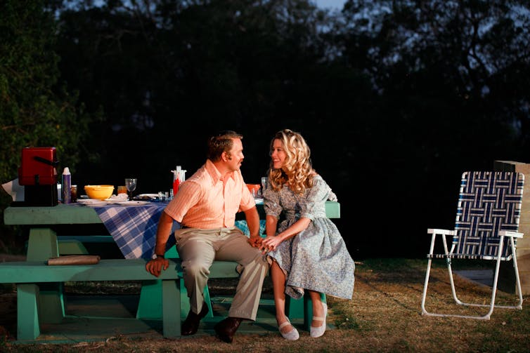 Production image: two characters in 80s dress outside.