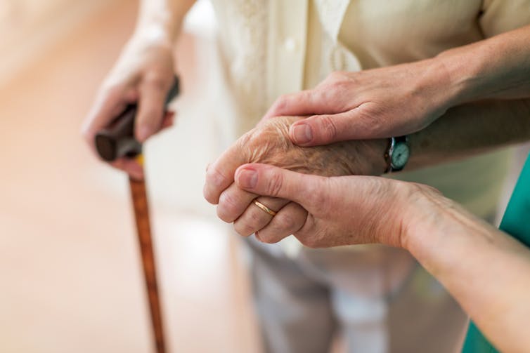 A carer holds the hand of an elderly person.