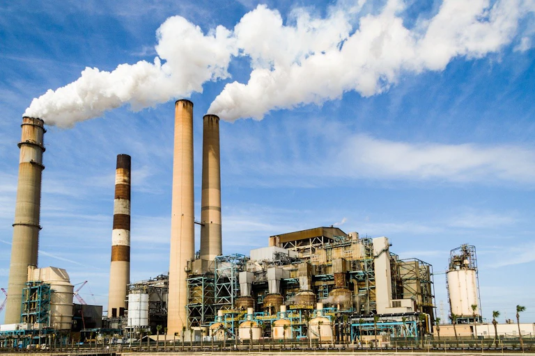A gas power plant emitting thick, white smoke with clear blue skies in the background.