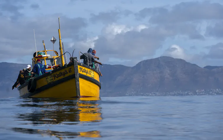 A small yellow fishing vessel sails in calm coastal waters.