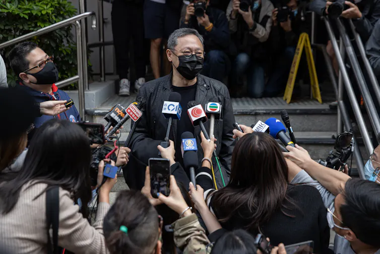 A man with a mask talking with journalists in Hong Kong.