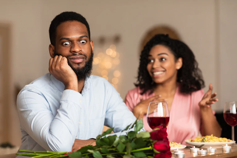 A man looks away from a speaking women with an amusing expression of boredom