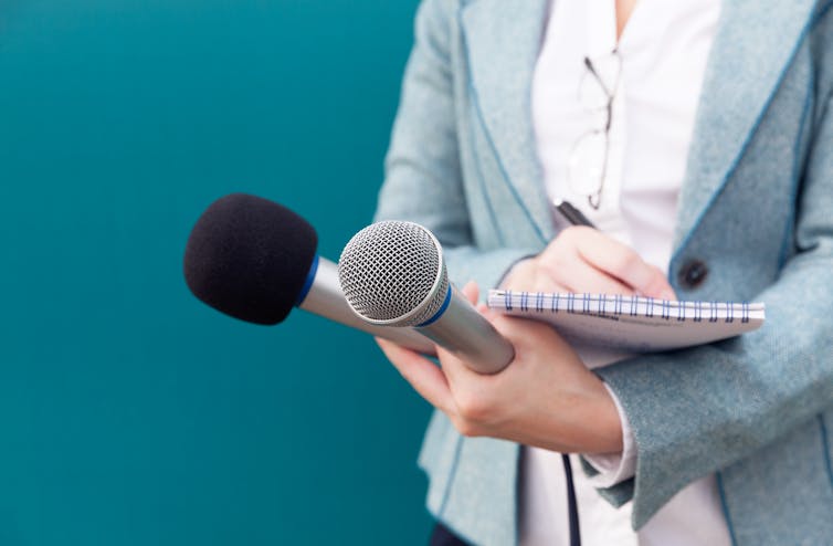 A woman holding two microphones and a reporter's pad.