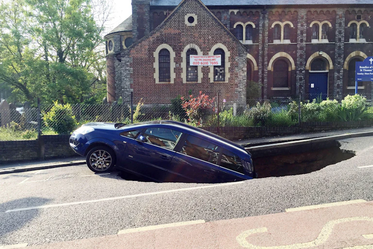 A blue car falling into a sinkhole in the road. Church in background.