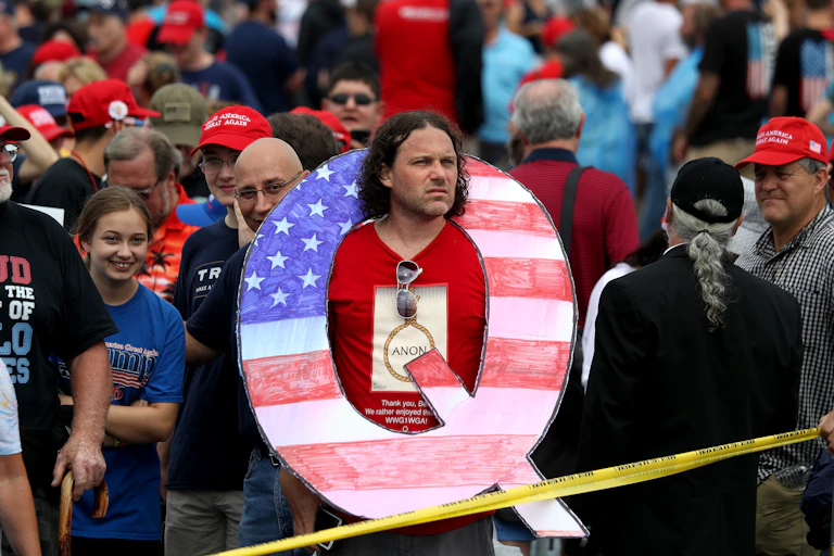 A Trump supporter at a rally wears a giant cutout 'Q.'