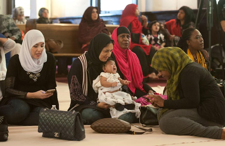 Muslim women and a baby waiting for prayer service in mosque while sitting on the floor