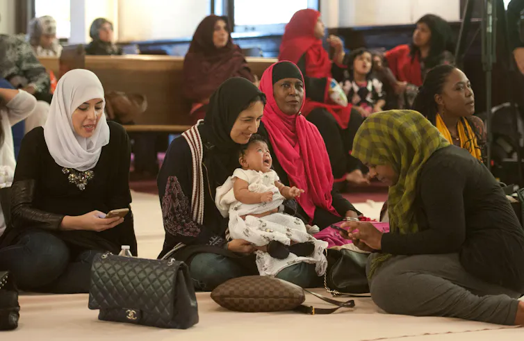 Muslim women and a baby waiting for prayer service in mosque while sitting on the floor