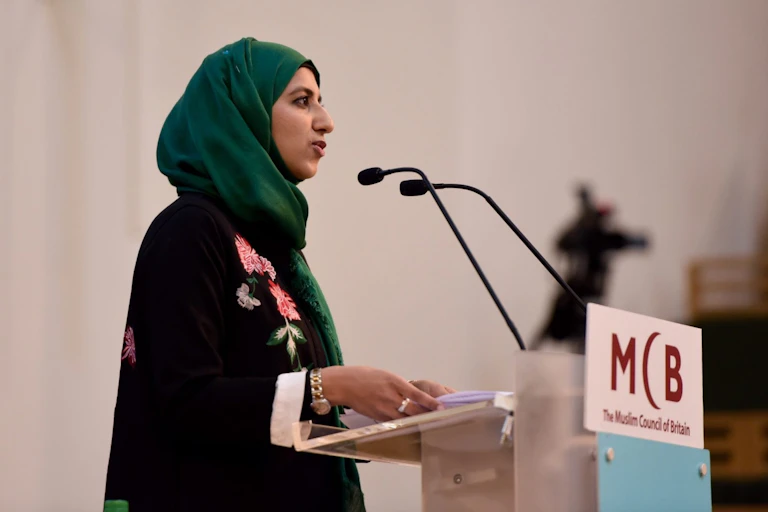Woman giving speech at a podium with a logo that reads: MCB The Muslim Council of Britain