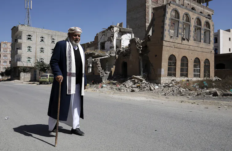 A man with a walking stick walks past a bombed building in Sana'a, Yemen, February 2021.