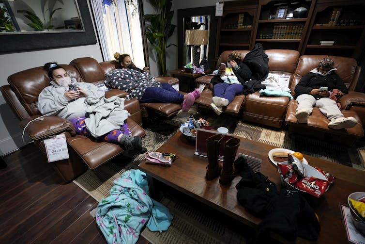 People bundled in blankets sit on chairs in a furniture showroom.