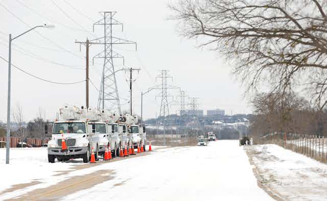 Service trucks parked under power lines in snow. 