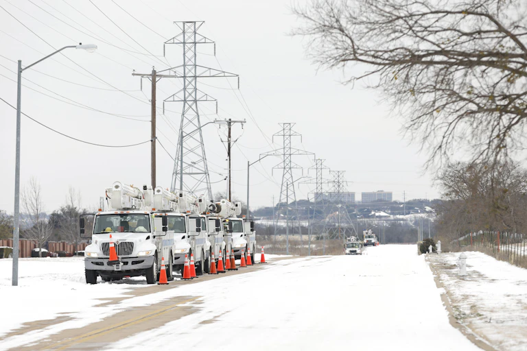 Service trucks parked under power lines in snow.