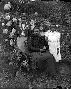 A woman poses with her stylishly dressed daughters in a lush garden.