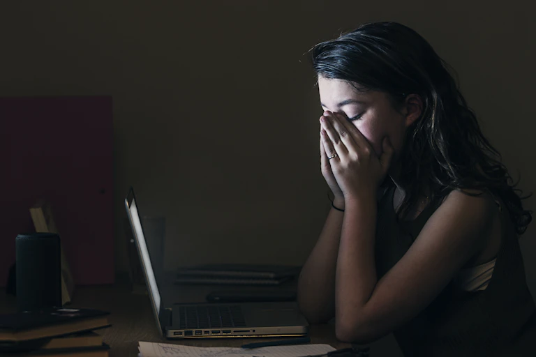A young woman horrified at what she sees on her computer.