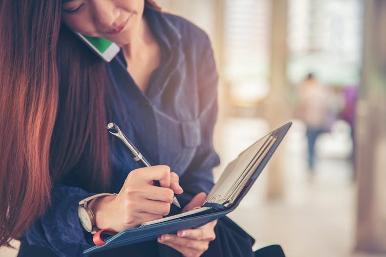 young women on phone makes an entry in her diary