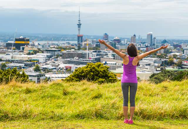 A women doing exercise on a green hill overlooking Auckland city.