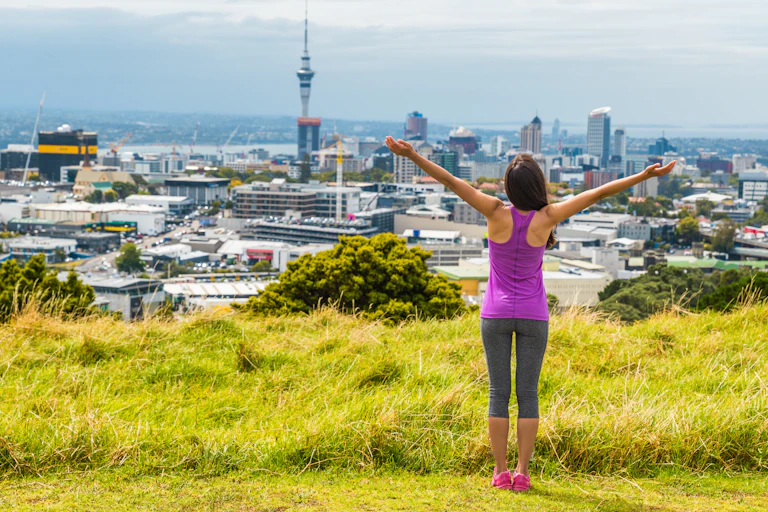 A women doing exercise on a green hill overlooking Auckland city.