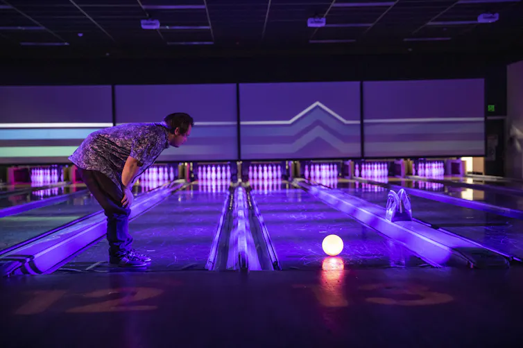 A man leans over a glowing bowling ball.