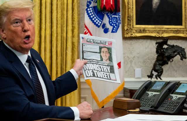 Donald Trump in the White House holds up a copy of the New York Post with a front page about his use of Twitter.