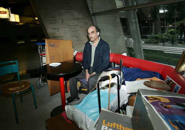 A man sits near his gear on a red bench in an airport terminal.