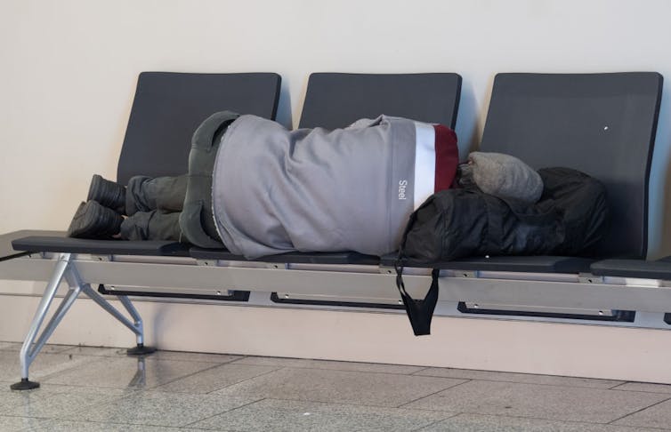 A man sleeps on chairs in an airport.