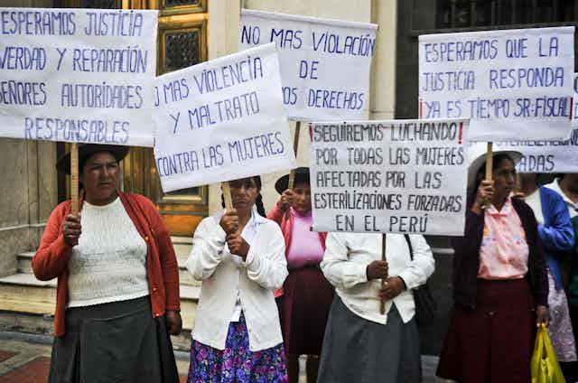 Half a dozen women in Andean dress hold signs decrying forced sterilization on a city street